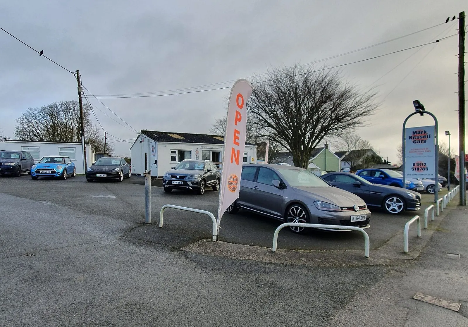 Mali auto salon s rabljenim automobilima na parkiralištu i zastavom s natpisom Open